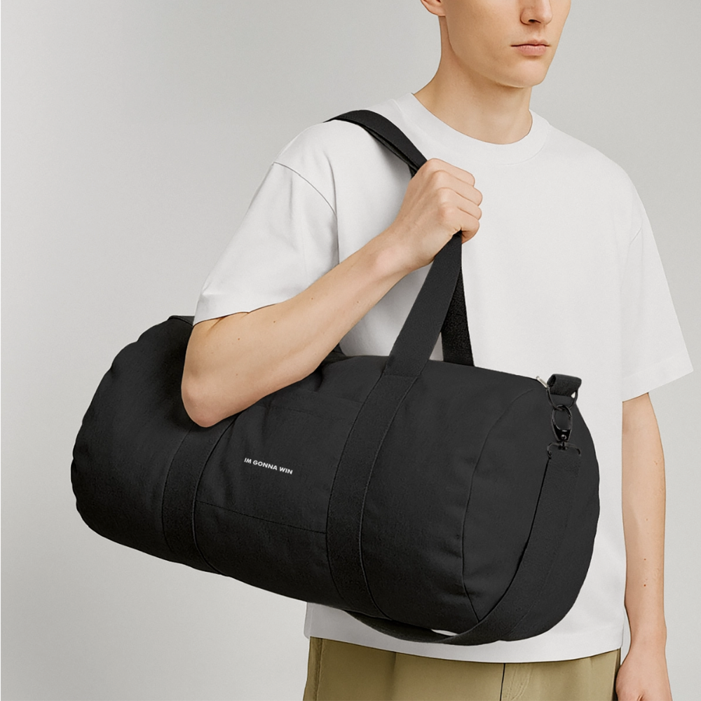 Person med hvid T-shirt bærer en stor sort sportsstasæk på skulderen.