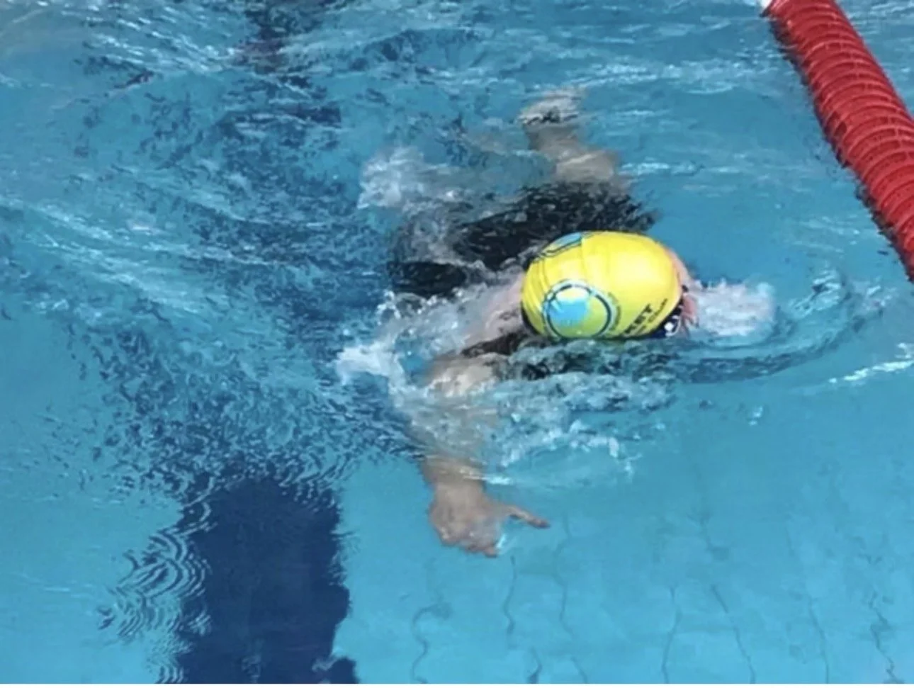Triathlete swimming front crawl in a pool wearing a yellow swim cap