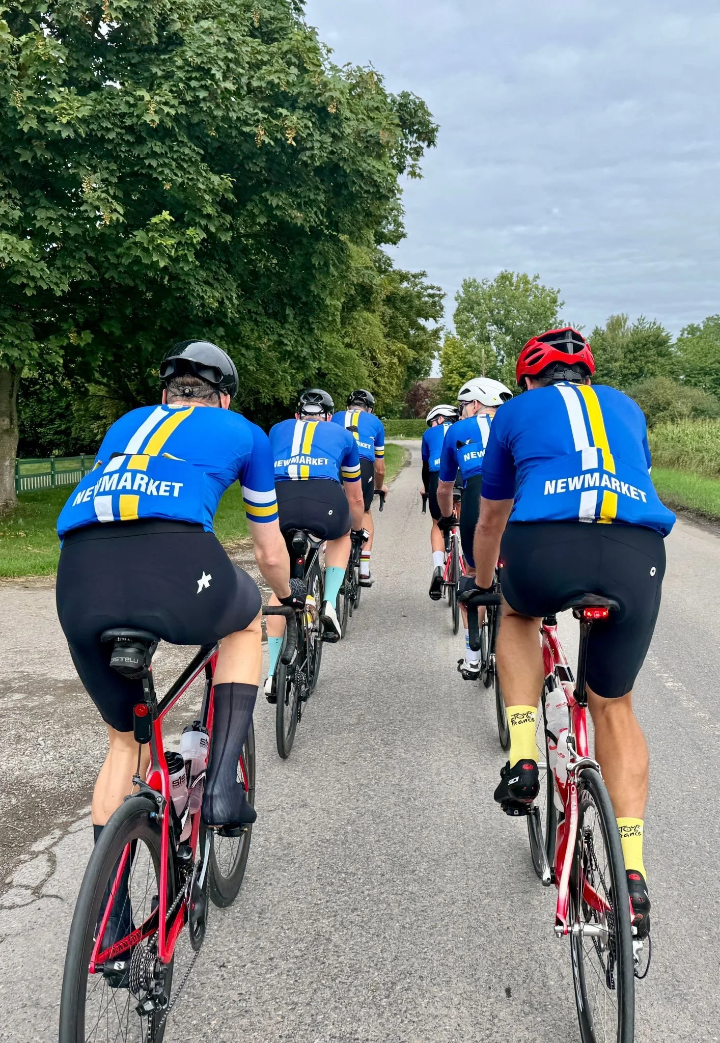 NC&TC riders in blue and yellow club kit on a Saturday group ride along a tree-lined lane