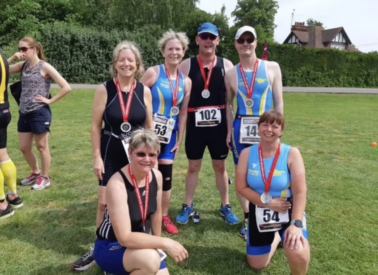 Smiling NC&TC triathletes with finisher medals and race numbers after a triathlon