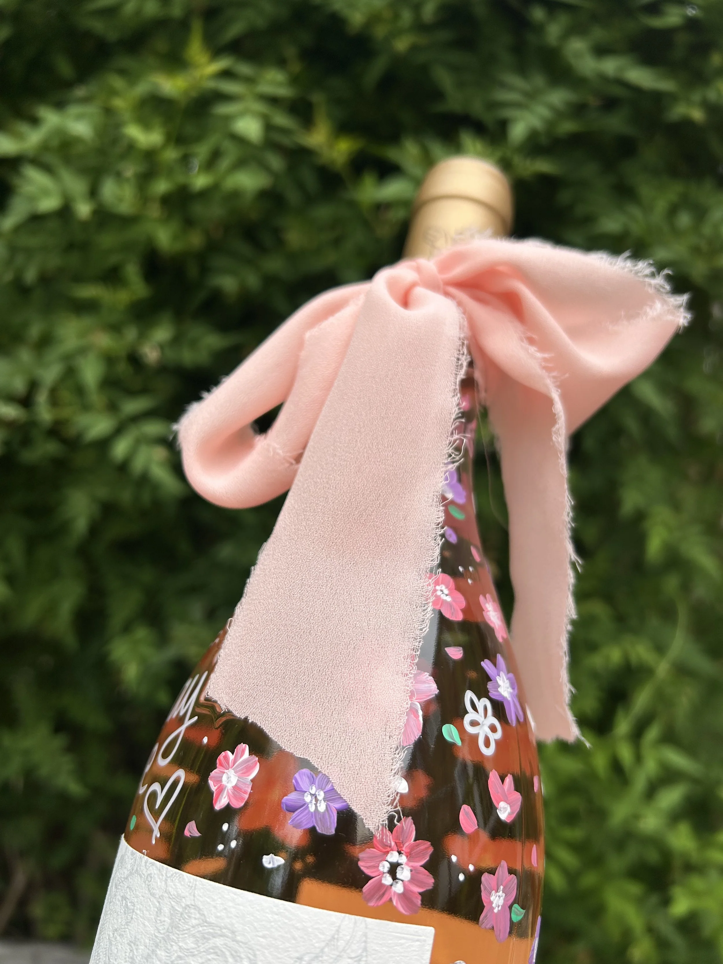 A photograph of a bottle of Whispering Angel rosé with hand painted pink and purple florals, complete with a pink bow tied around the neck of the bottle.