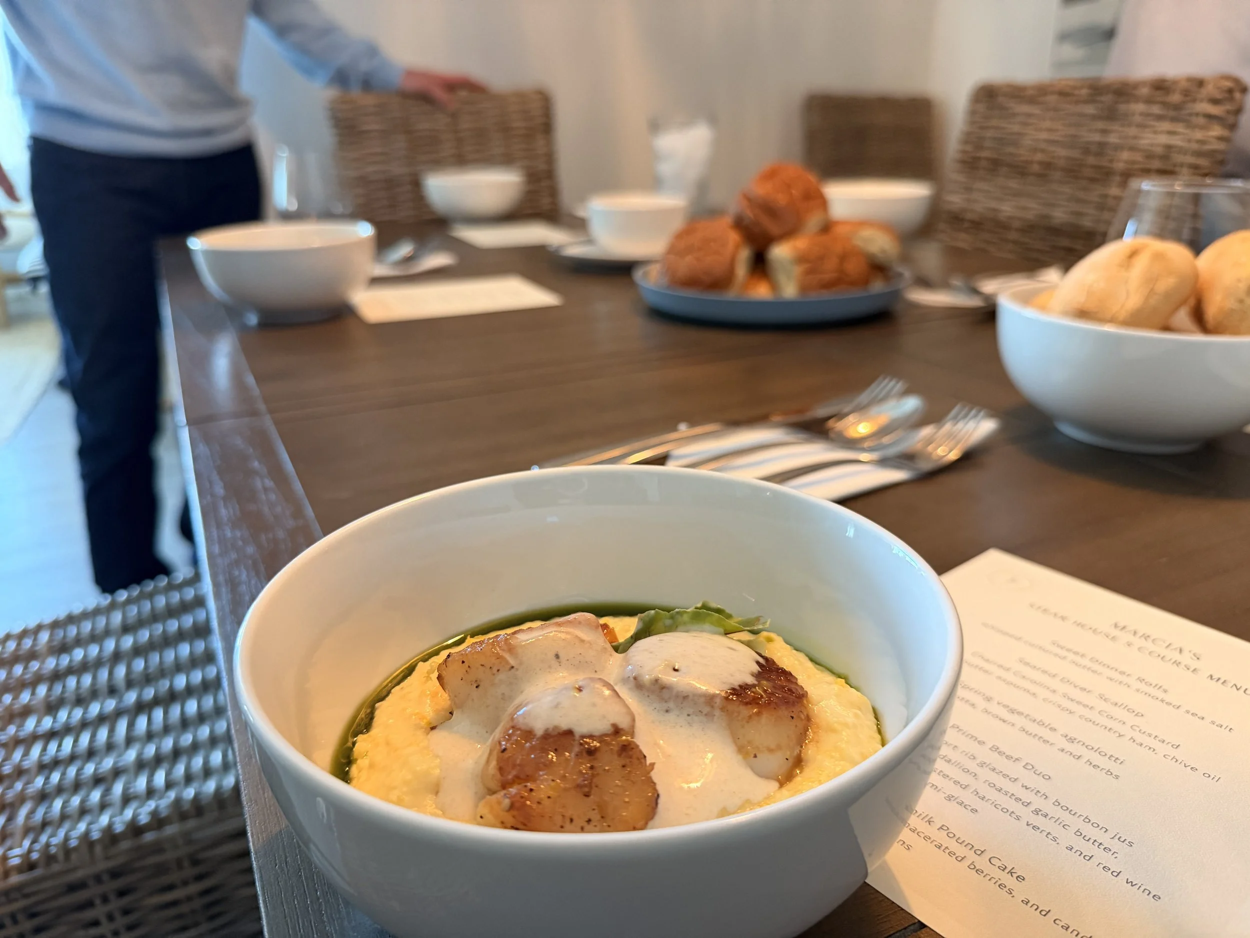A bowl of breakfast with eggs, sausage and vegetables on a table set for a meal.
