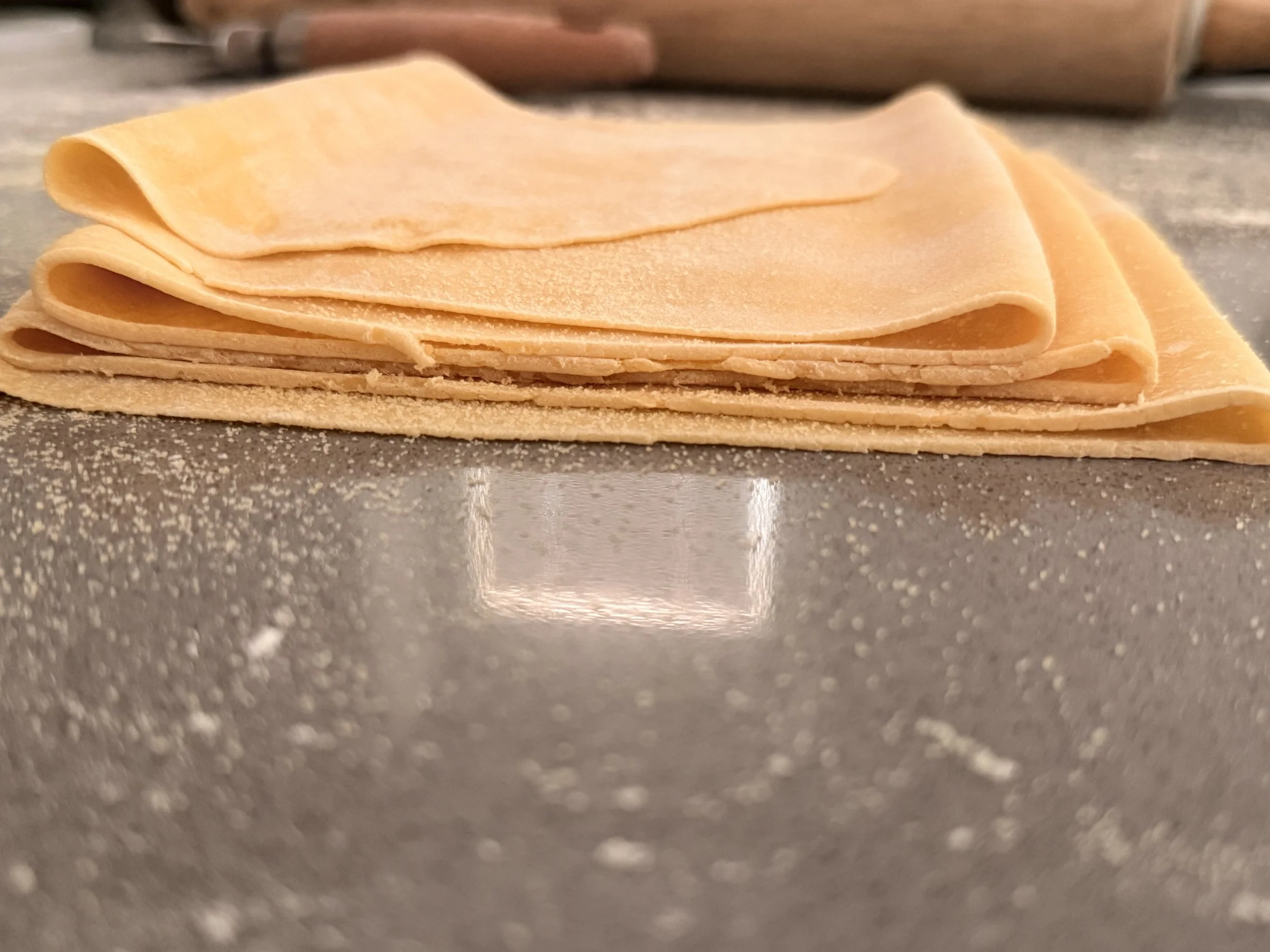 Stack of uncooked lasagna noodles on a floured gray surface.