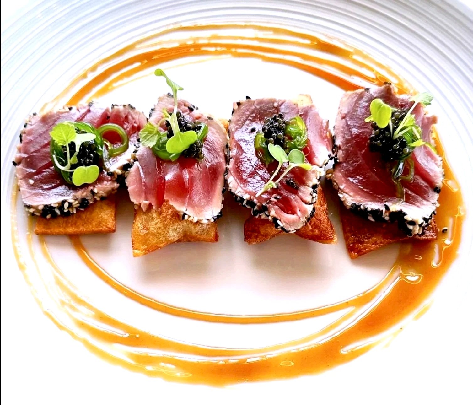 Tuna tartare served on crispy crackers, garnished with microgreens and black caviar, with a decorative sauce ring on the plate.