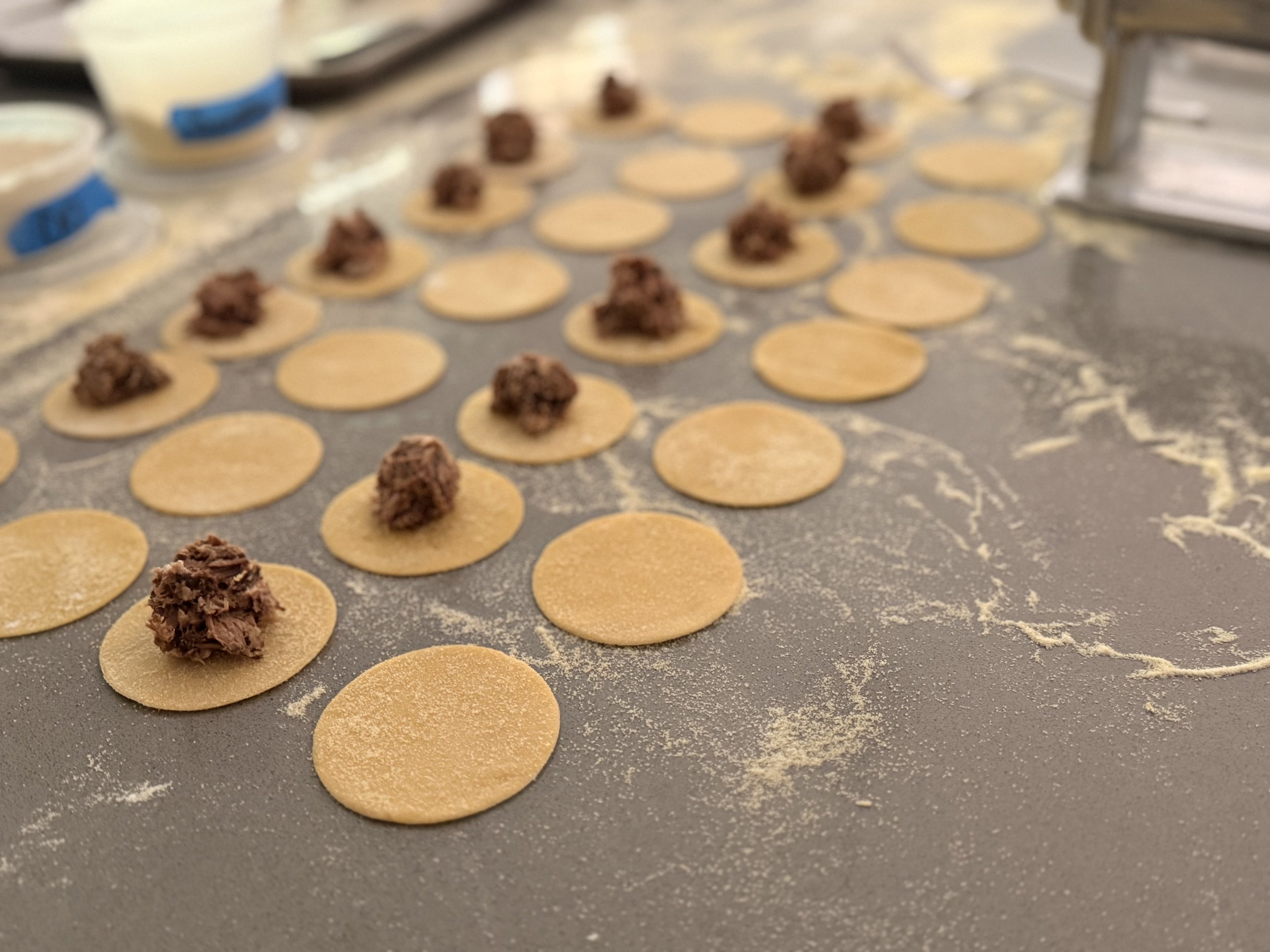 Unbaked cookies with chocolate filling on a gray baking sheet with some flour dusted on it.