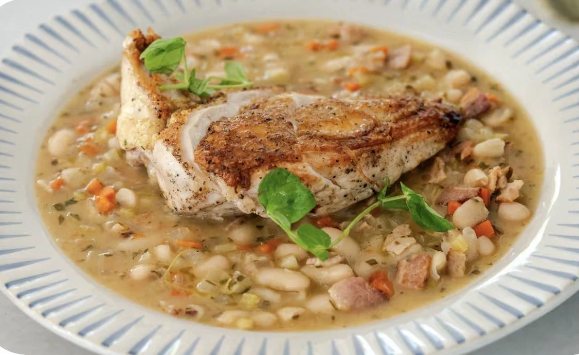 A plate of baked fish served with a side of vegetable and bean stew.