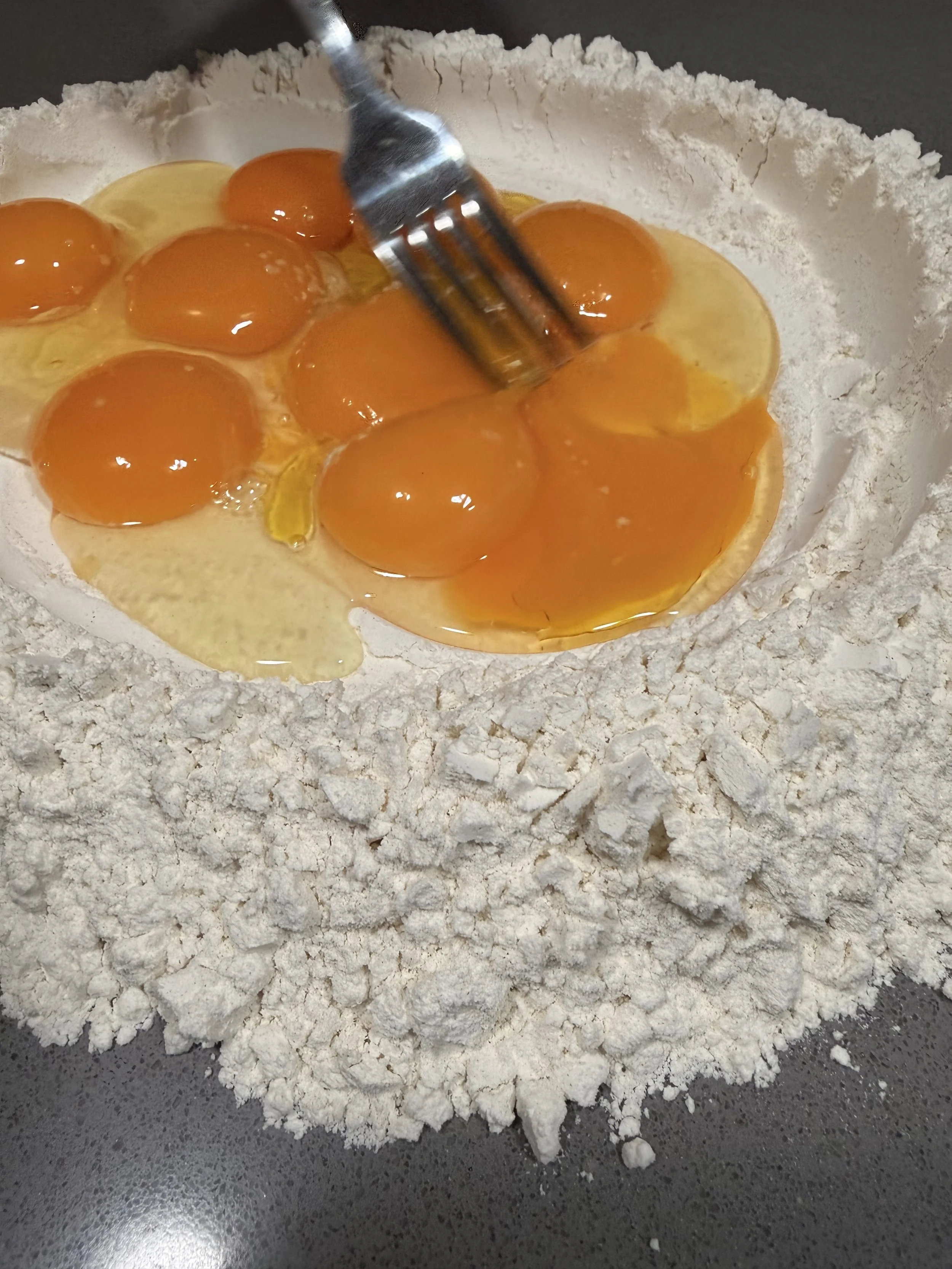 A mixture of eggs on top of flour in a bowl, with a fork, ready for baking.
