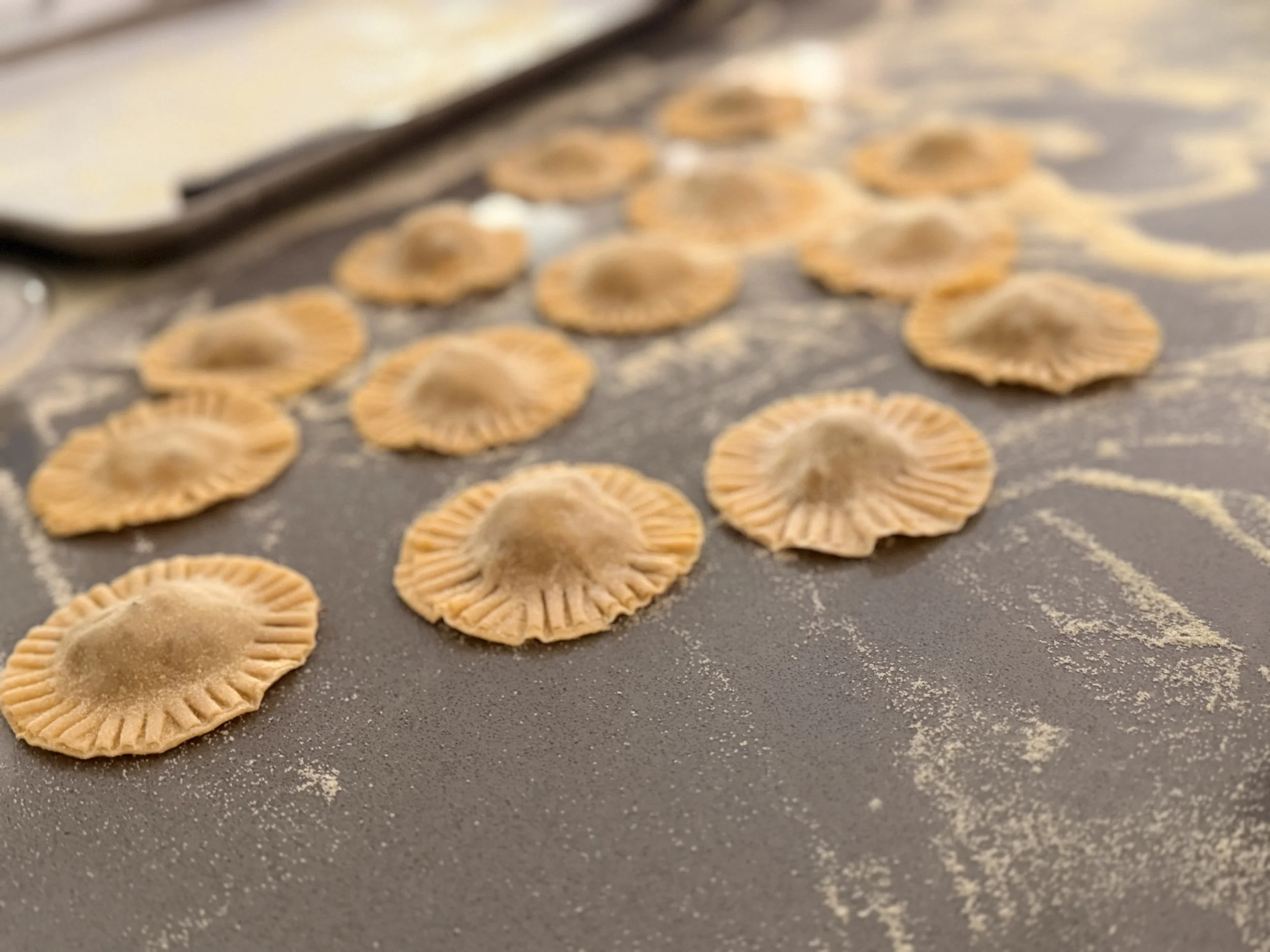 Close-up of dried pasta shells on a floured surface with a metal utensil nearby.