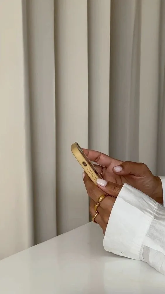 Close-up of a person's hand holding a gold-colored smartphone with a curtain in the background.