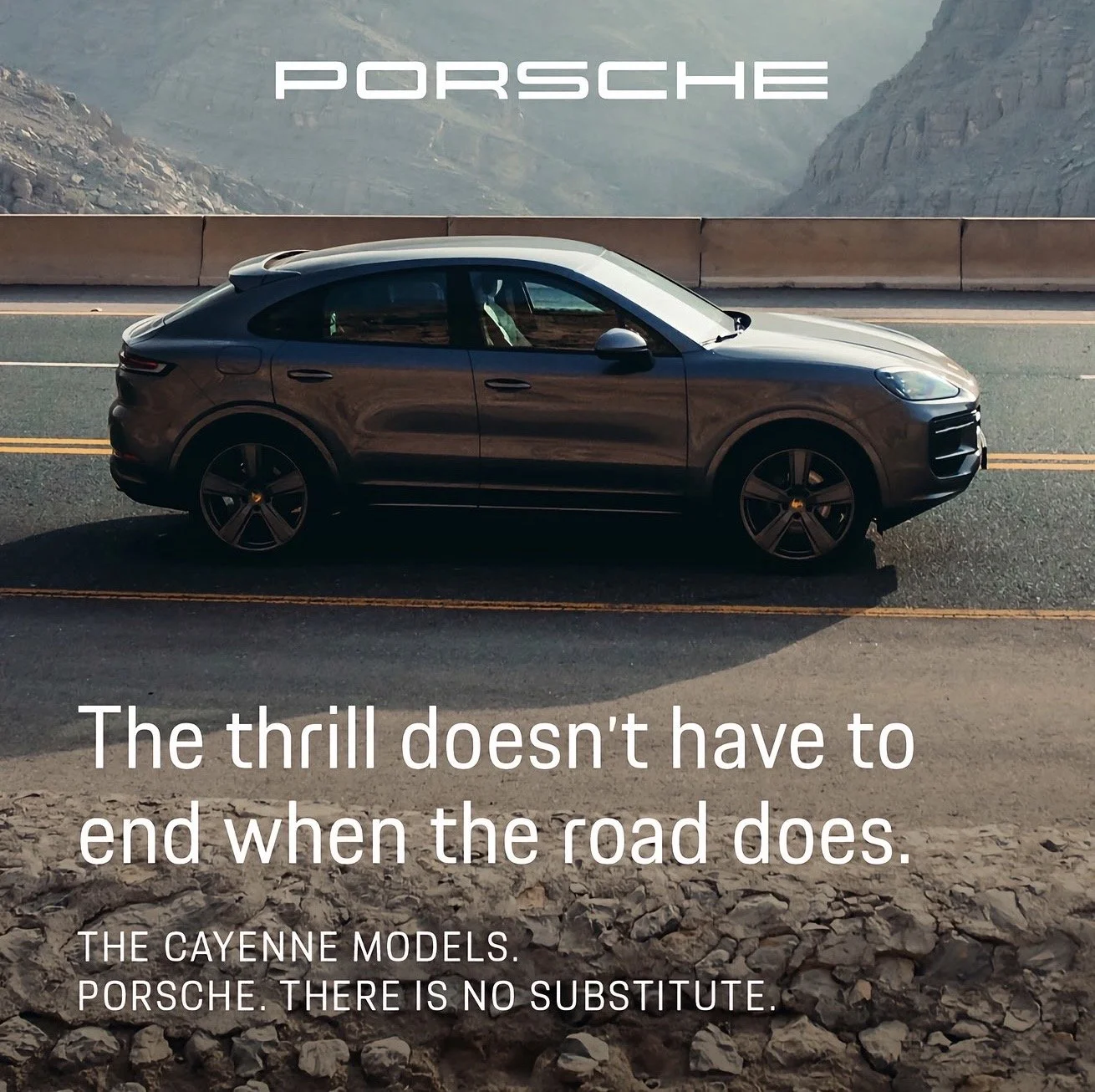 A sleek black Porsche Cayenne model parked on a mountain road with a view of rocky mountains in the background. There is a large Porsche logo at the top and text at the bottom that reads, 'The thrill doesn’t have to end when the road does. The Cayenn