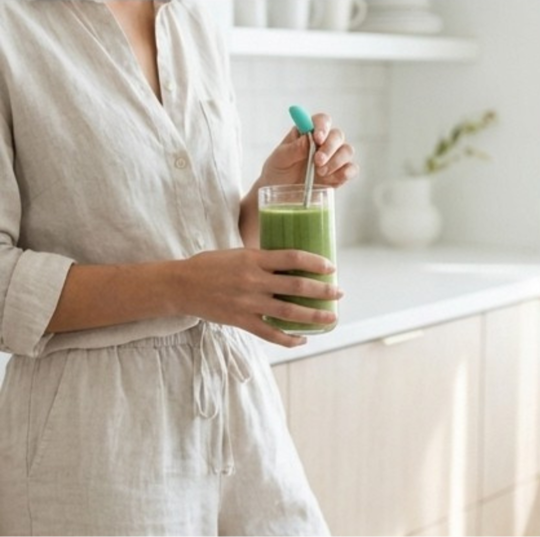image of a female body in linen outfit holding a green juice drink in kitchen with stainless streel straw and wrinx straw attachment
