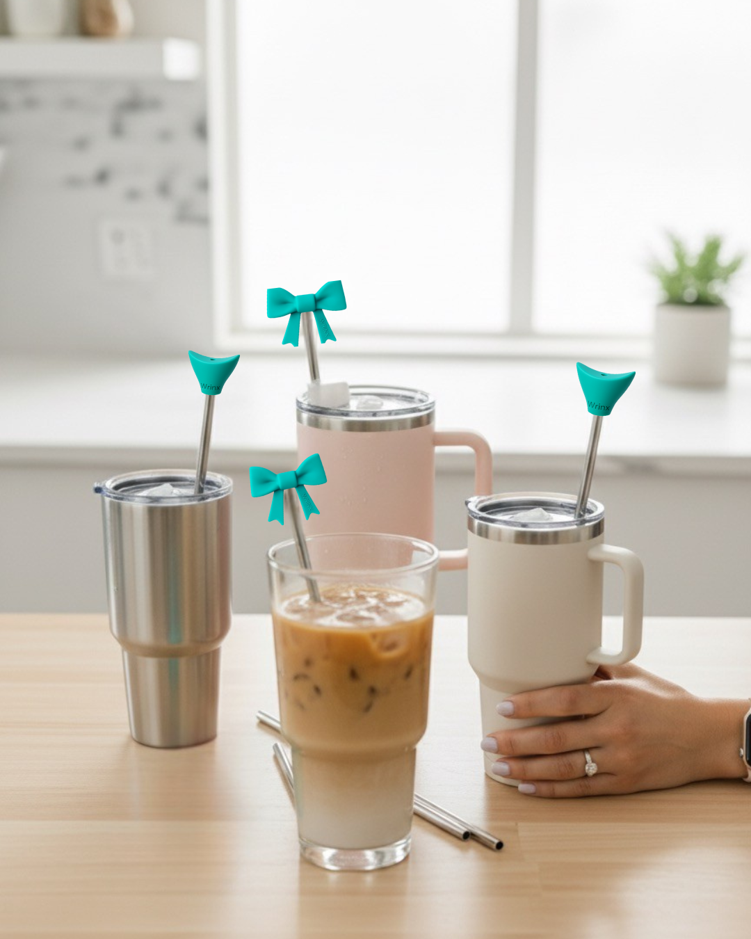 4 cups on a wood kitchen counter. 3 tumblers and one class cup filled with coffee. all with stainless steel straws and teal wrinx straw attachments