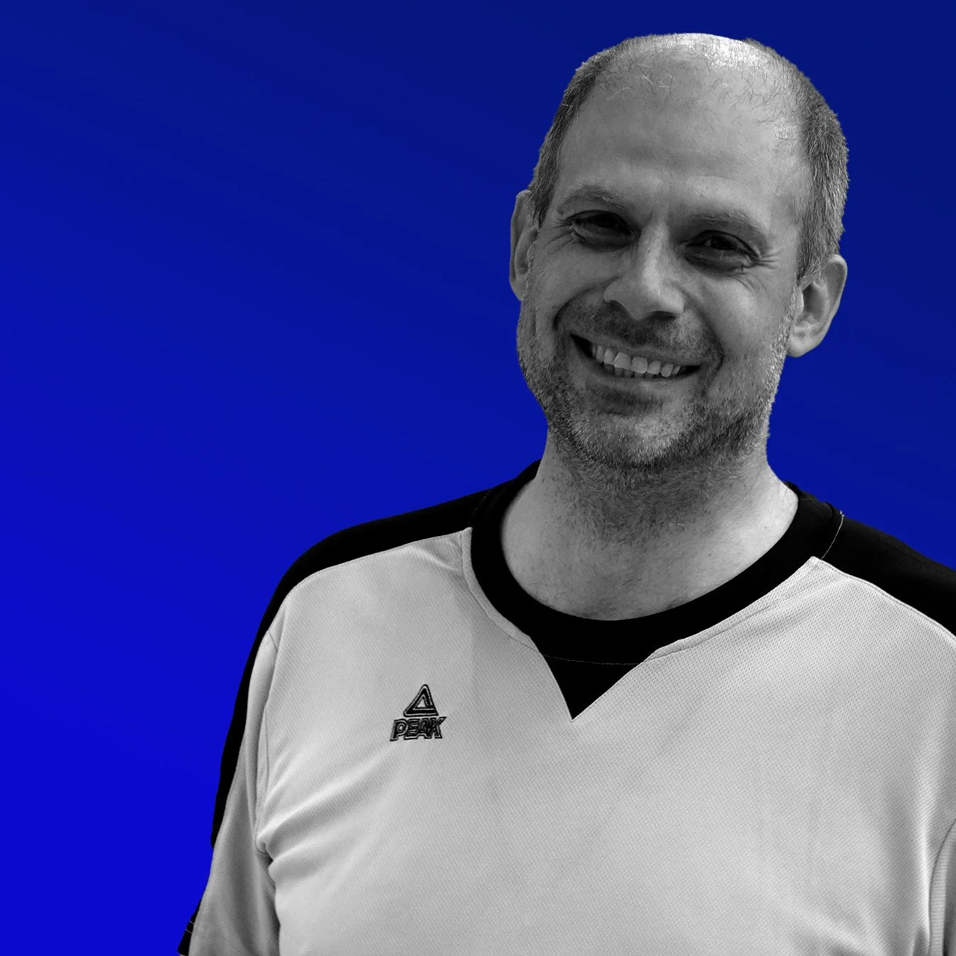 Ein lächelnder Mann in einem weißen und schwarzen Sportshirt vor einem blauen Hintergrund.