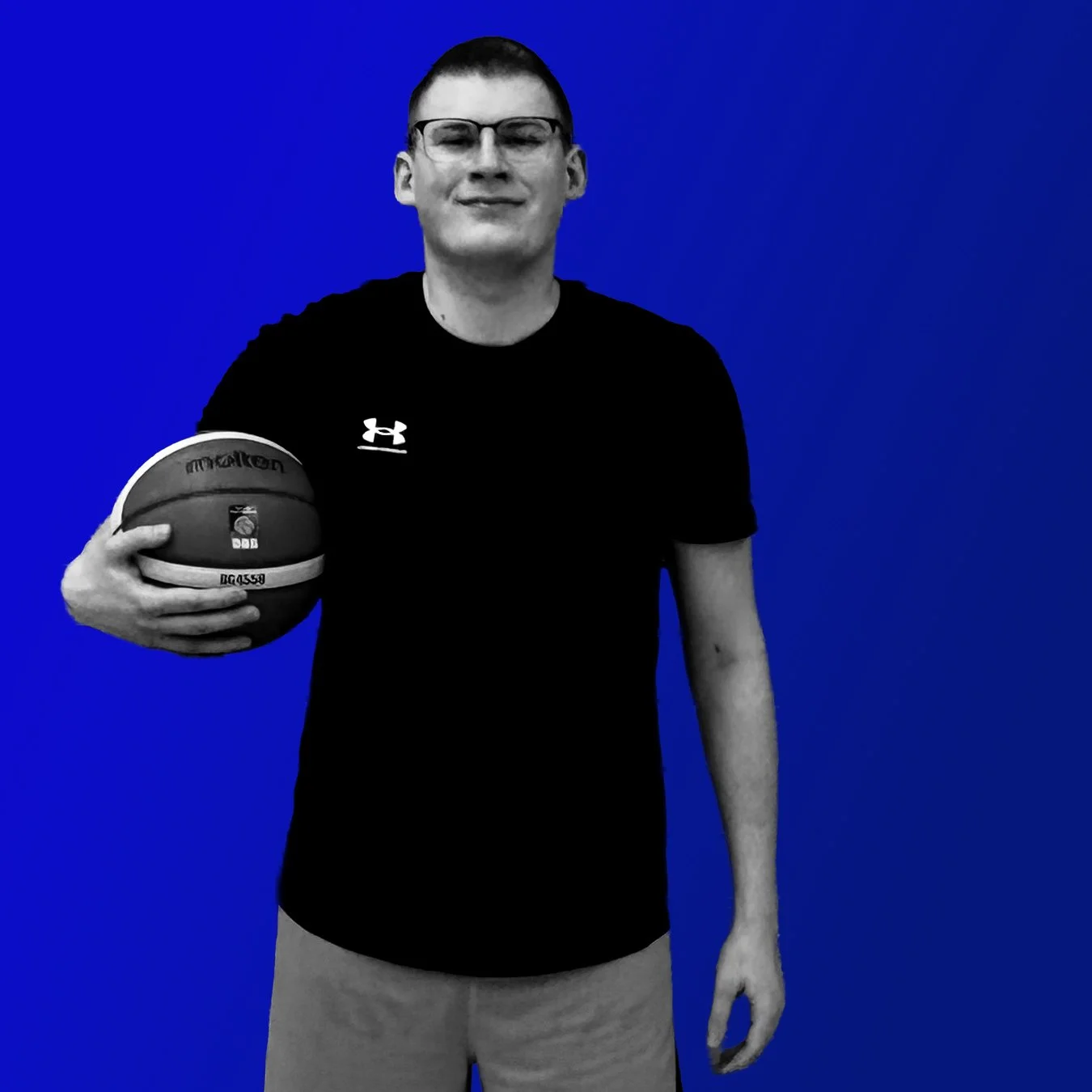 Jugendlicher Mann mit Brille hält einen Basketball vor einer blauen Wand