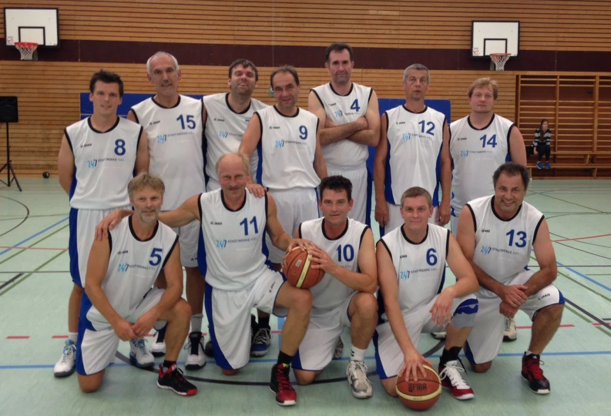 Eine Gruppe von Erwachsenen in Basketball-Uniformen auf einem Basketballfeld in einer Turnhalle.