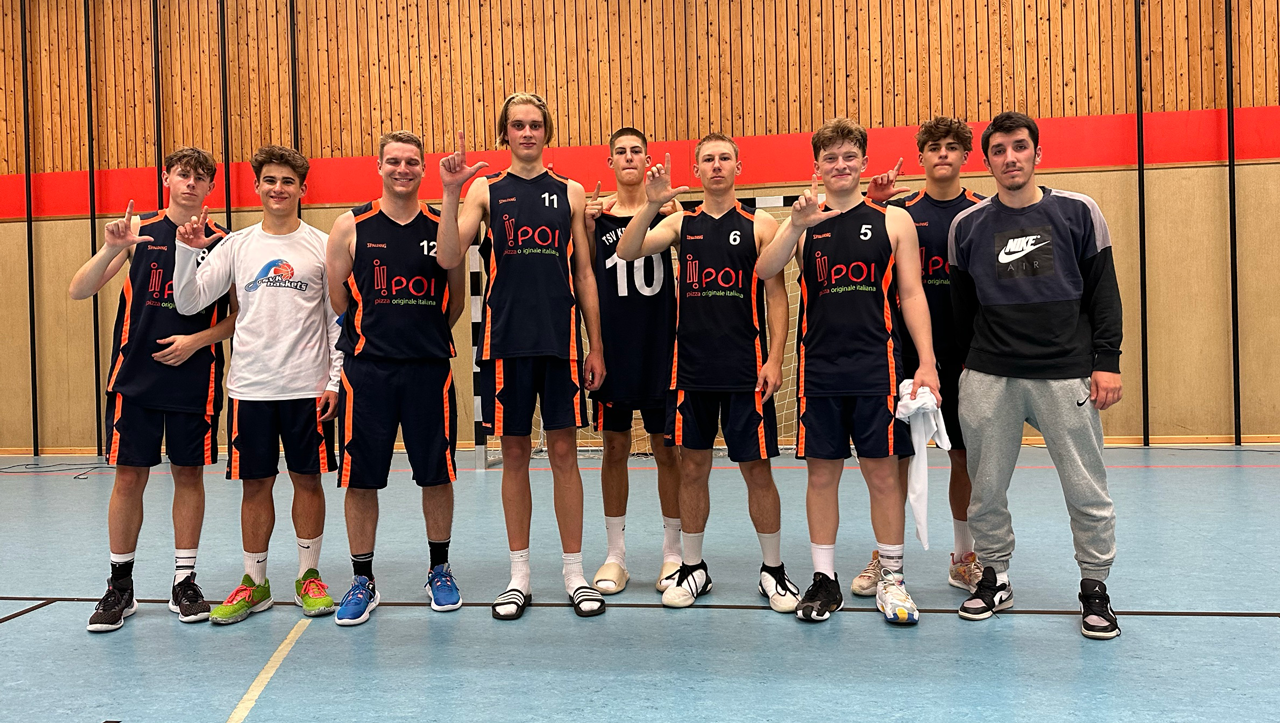 Eine Gruppe junger Männer in Volleyballtrikots und Hosen posiert in einer Turnhalle.