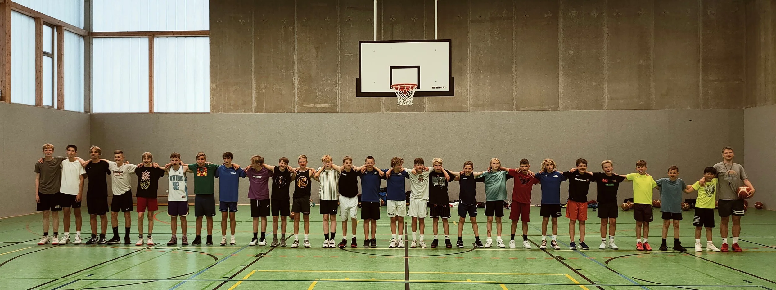 Gruppe von Jugendlichen in einer Turnhalle, die eine Basketballmannschaft bilden, mit einem Basketball in der Hand.