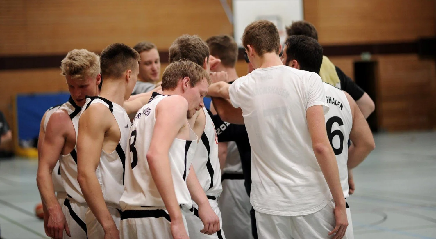 Junge Basketballspieler in Team-Kleidung versammelt sich in der Halle, um sich auf das Spiel zu konzentrieren.