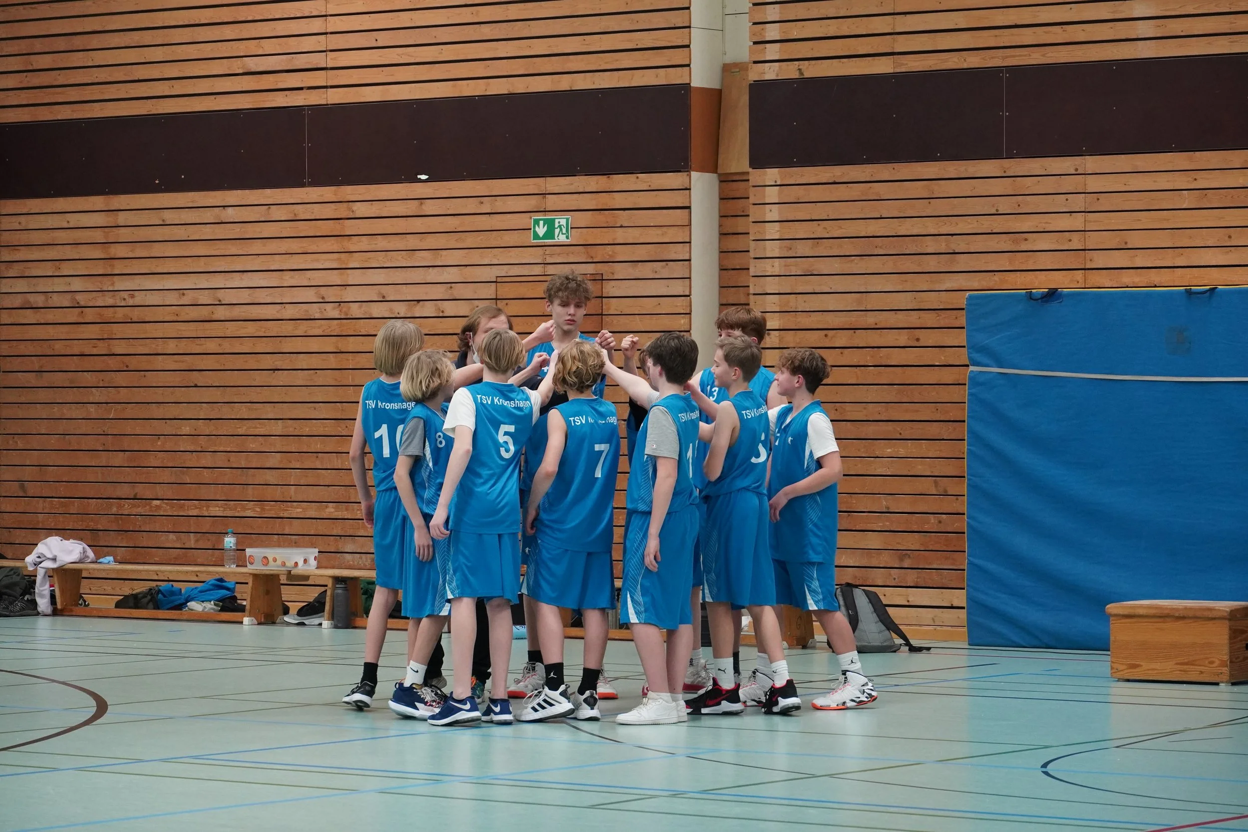 Jugendliche Basketballspieler in blauen Trikots versammeln sich in einer Turnhalle.
