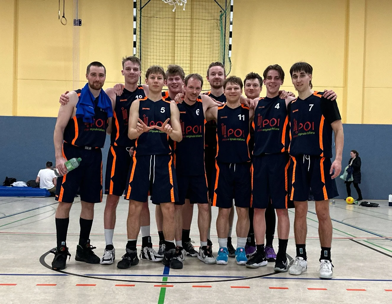 Ein Volleyballteam in schwarzen Trikots und Shorts posiert in einer Turnhalle.