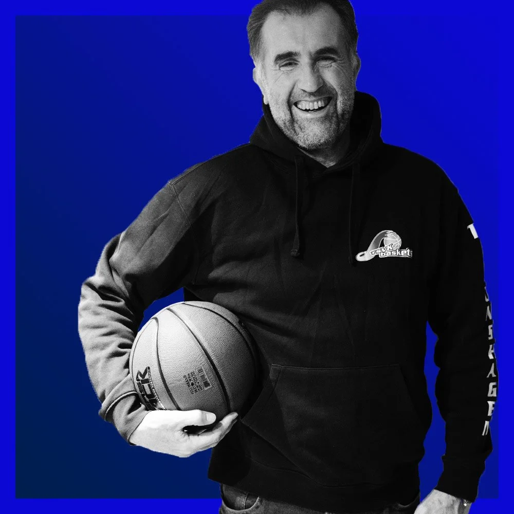Mann in schwarzem Hoodie mit Basketball in der Hand, lachend vor blauem Hintergrund