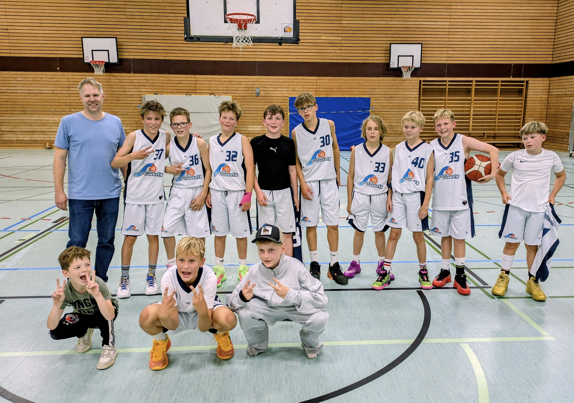 Junge Basketballspieler und ein Coach in einer Turnhalle für ein Gruppenfoto.