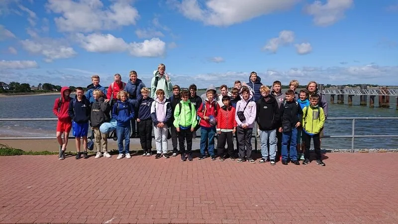 Gruppe von Kindern und Jugendlichen beim Ausflug am Fluss unter blauem Himmel.