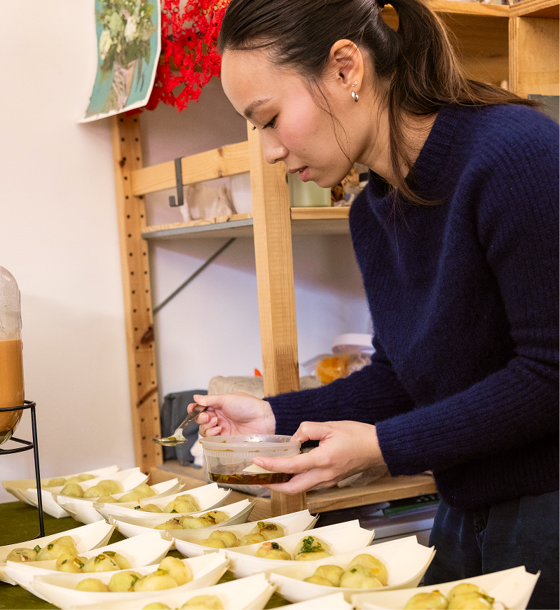 Christina, founder of Chenzi, adding savory sauce to Chenzi's Fuzhounese potato balls at an event.