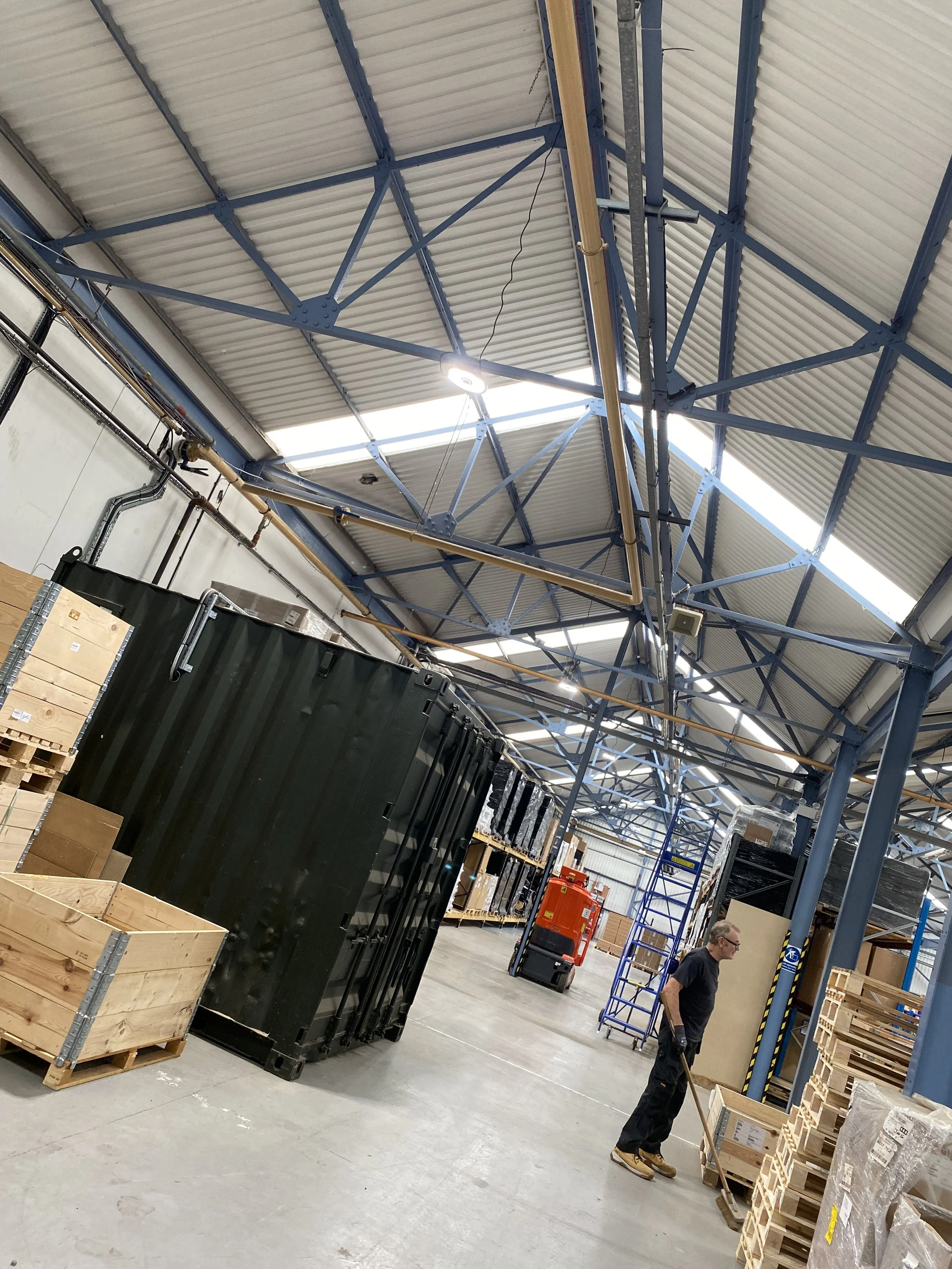 Wide view inside a warehouse with racking, pallets and an access platform, lit by bright LED warehouse lighting and natural light from rooflights.