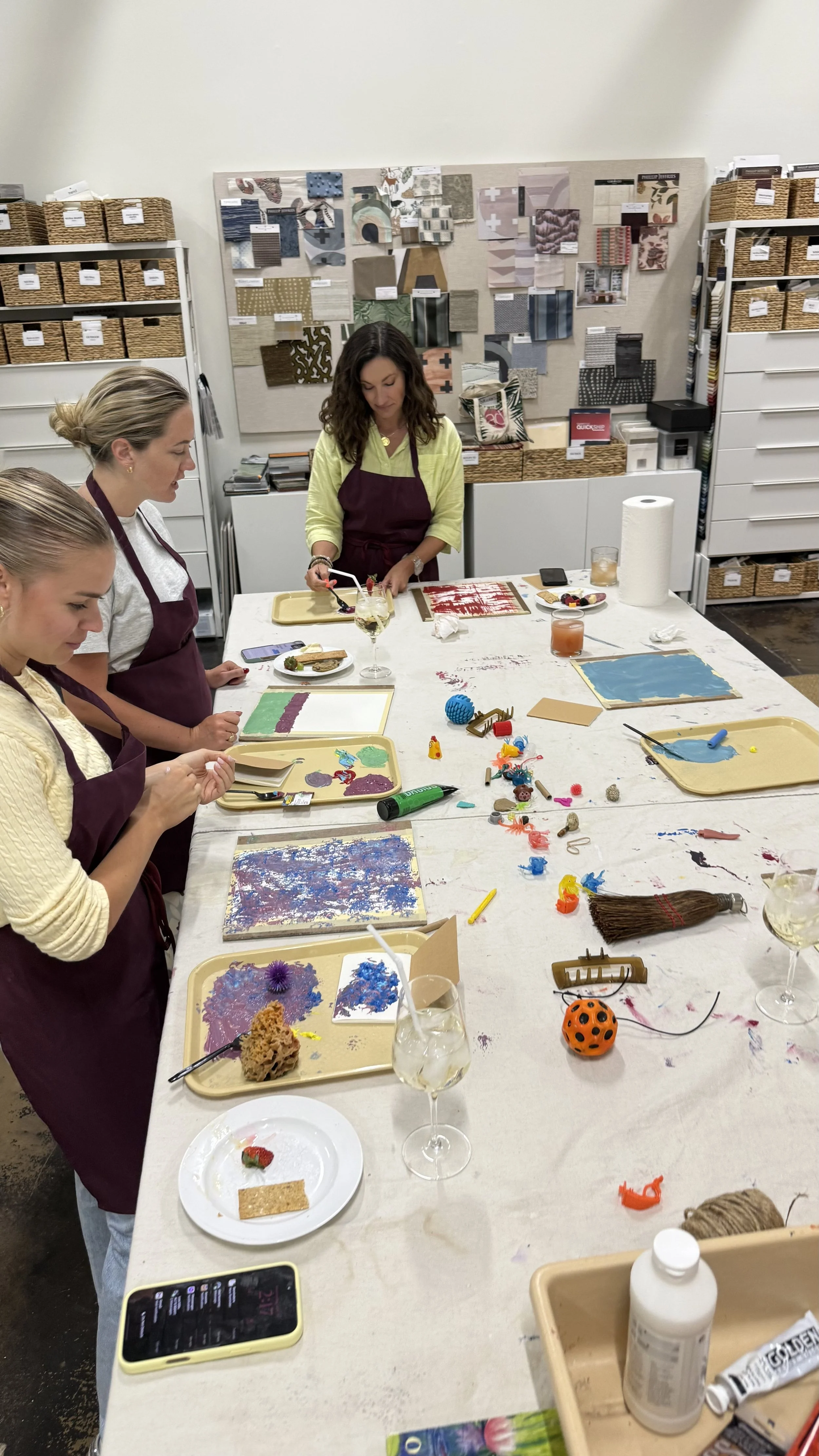 People gathered around a large table engaging in an art or craft activity, with various art supplies, paintings, and decorations on the table and in the background.