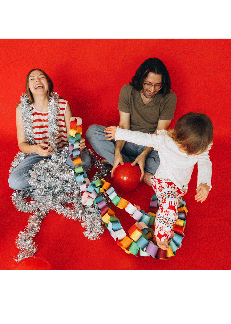A woman, a man, and a young girl enjoying a festive celebration with Christmas decorations and a red ball against a red background.