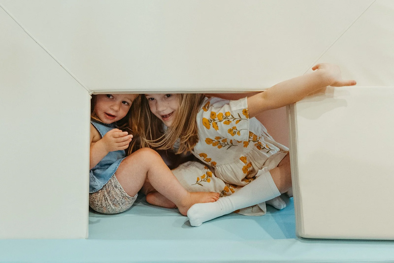 Two young girls playing inside a small enclosed space, smiling and interacting with each other.