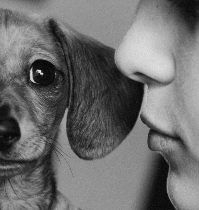 A person with their face close to a puppy, about to kiss or nuzzle it.