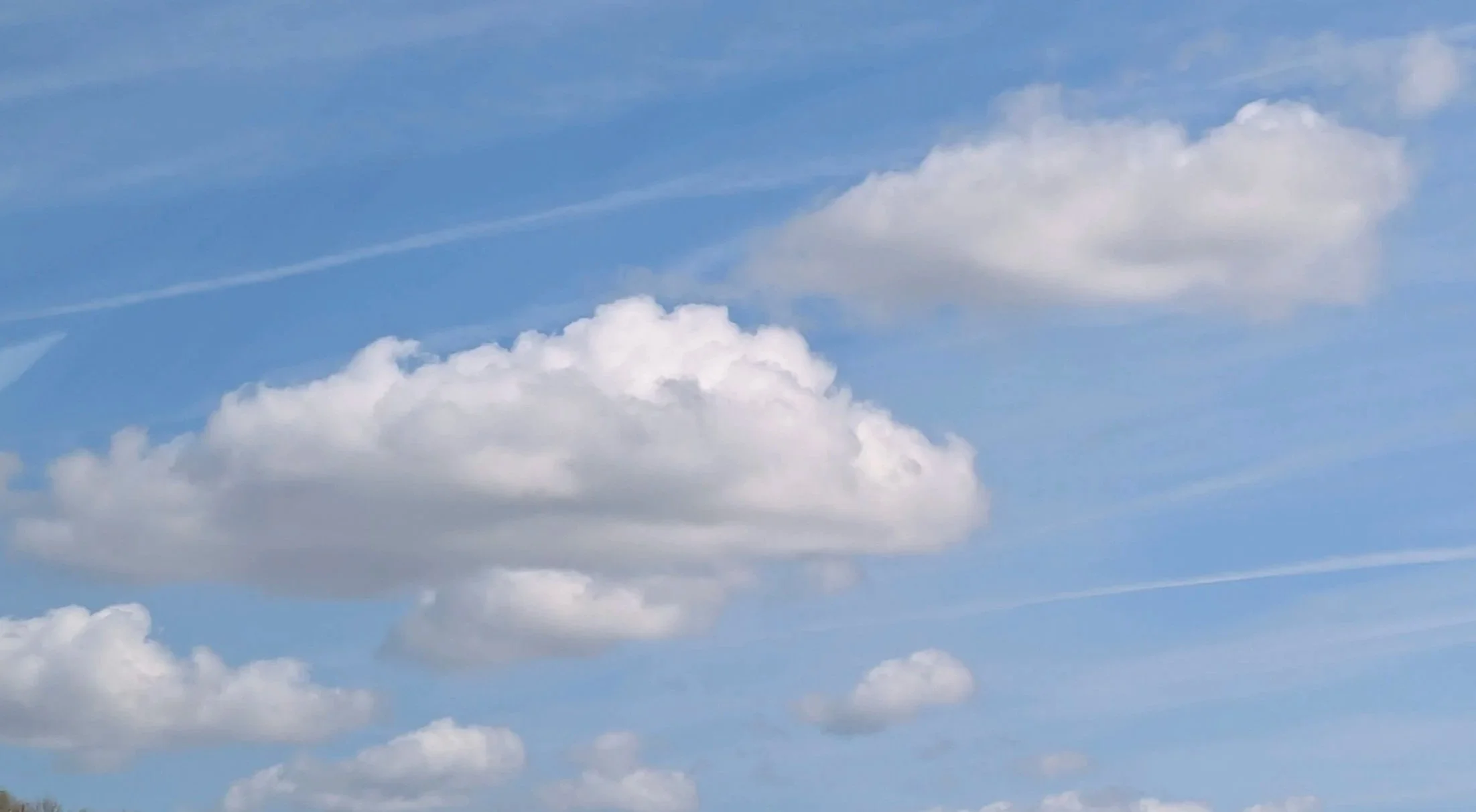 Blue sky with scattered white clouds and contrails.