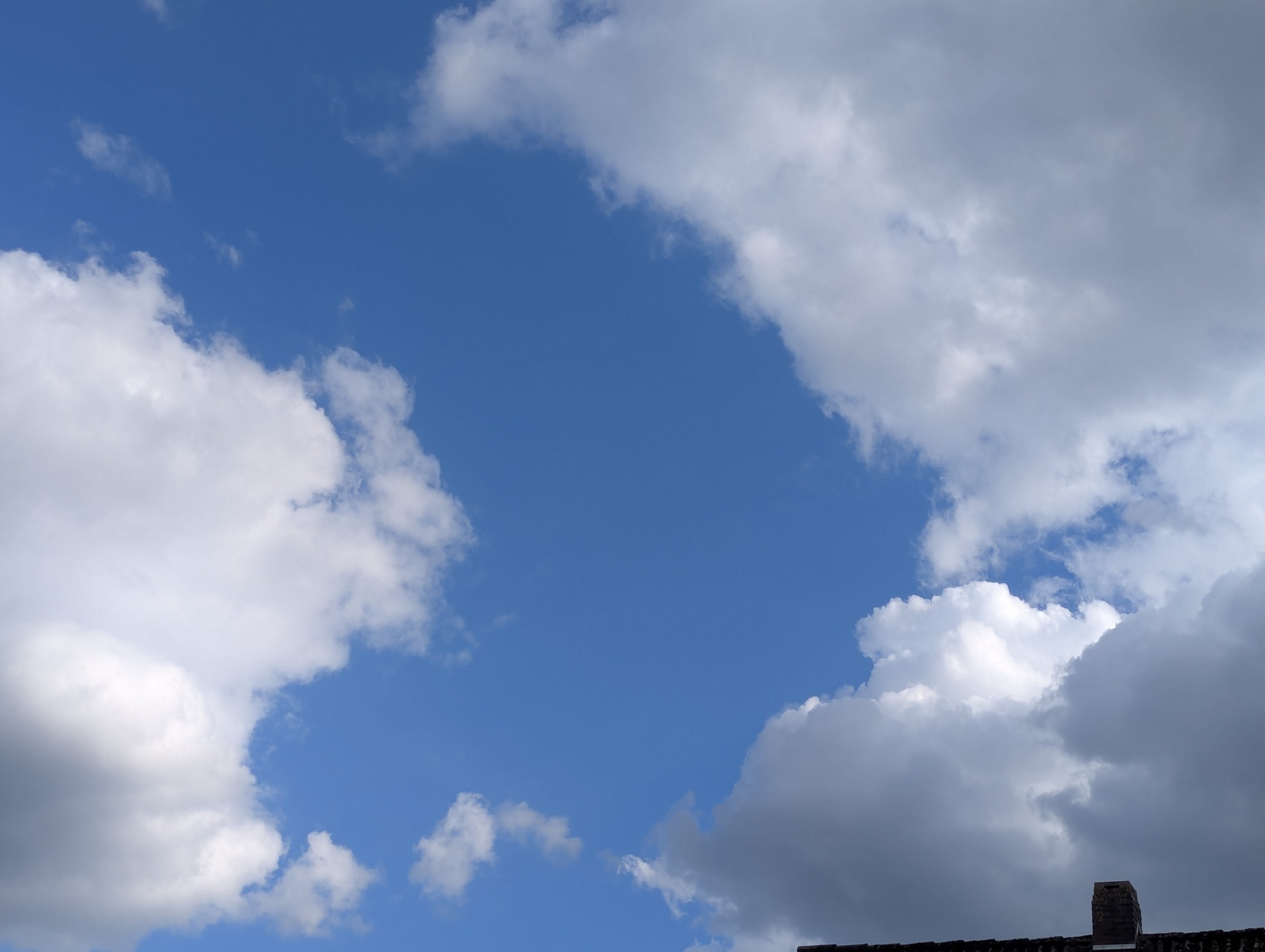Blue sky with scattered white clouds and a chimney in the bottom right corner.