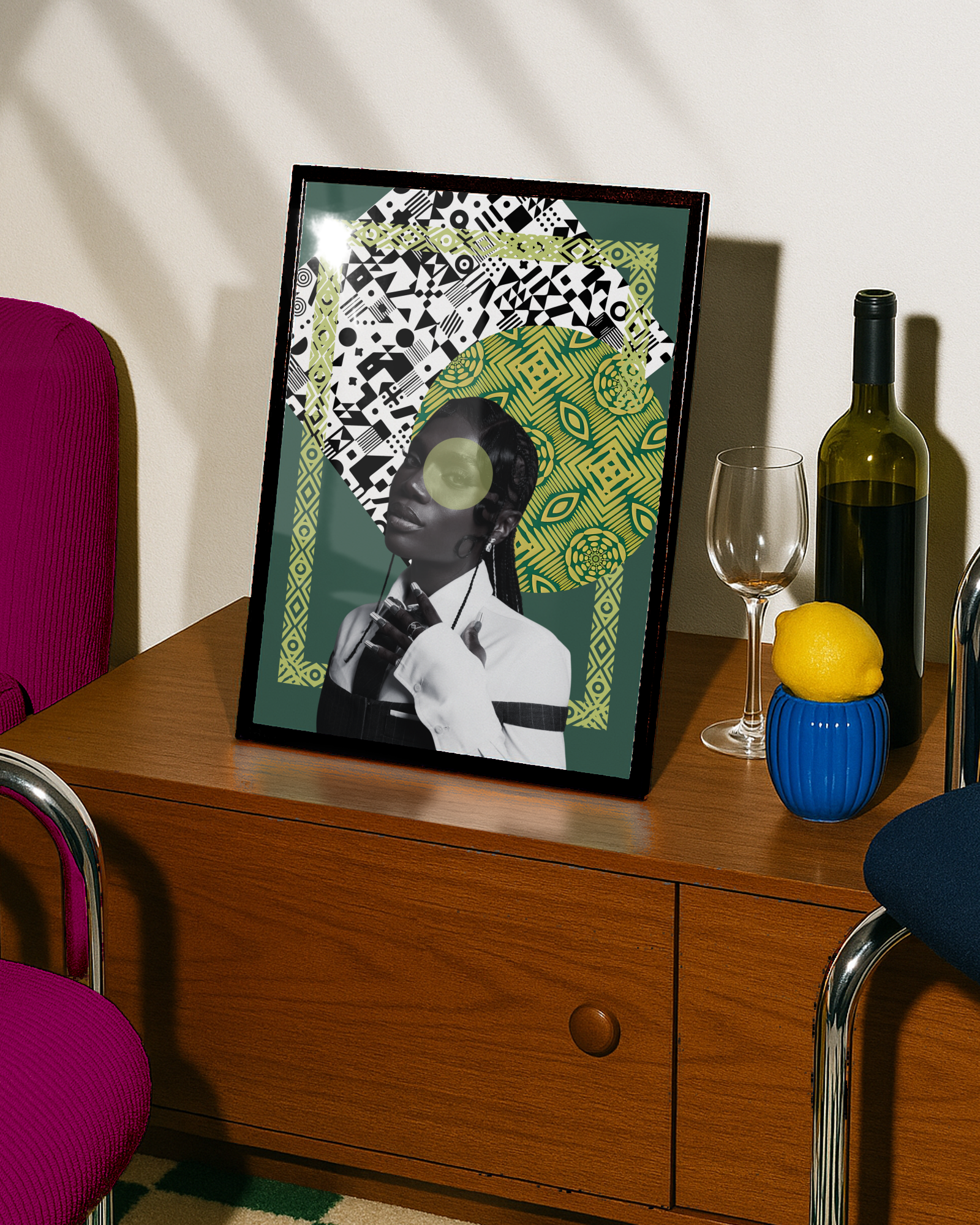 Decorative framed artwork on a wooden sideboard, featuring a black-and-white portrait of a woman with a patterned background consisting of black, white, and yellow-green designs, a wine bottle, empty wine glass, lemon in a blue vase, and a pink chair nearby.
