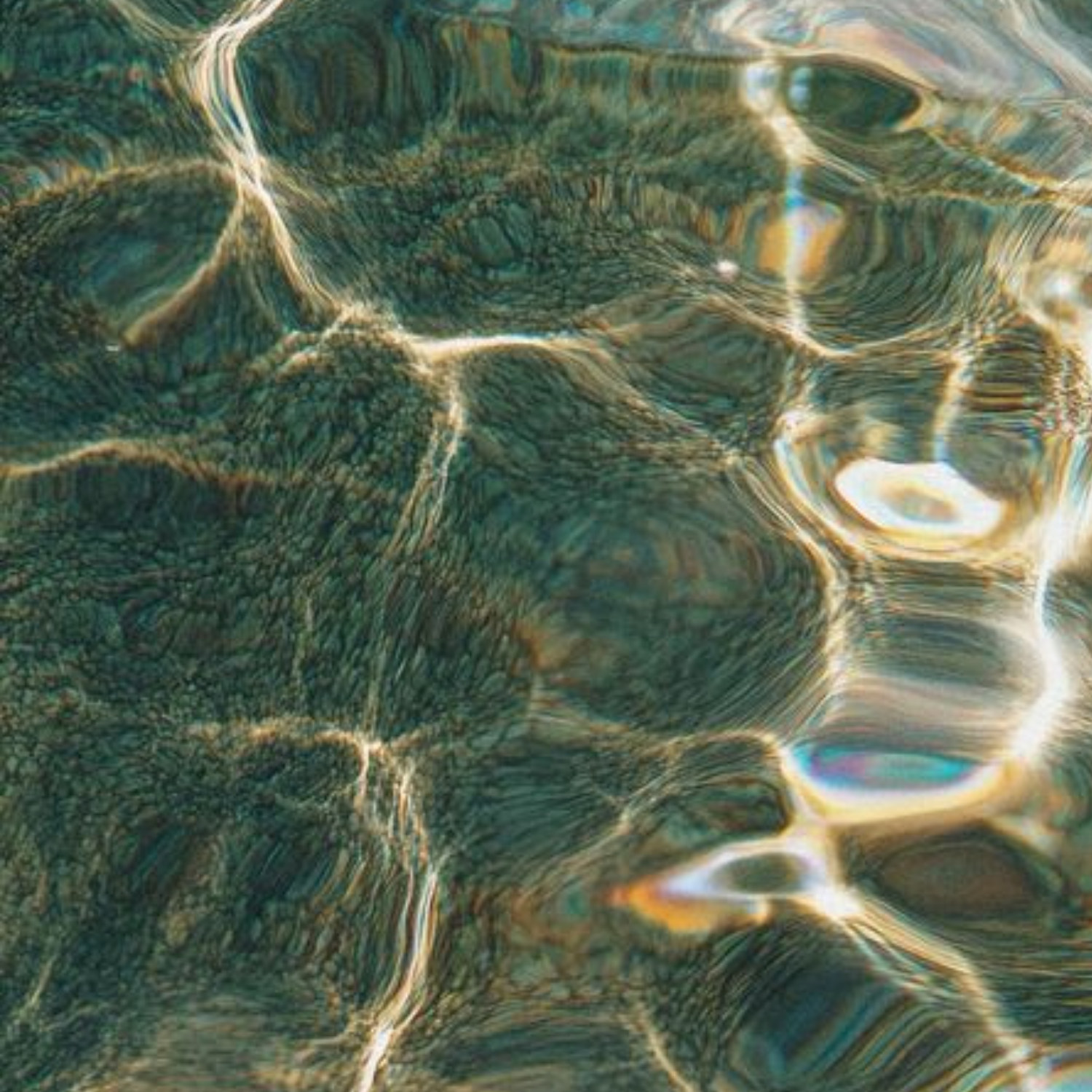 Close-up of water surface with sunlight reflections creating a pattern of ripples and shimmering light.