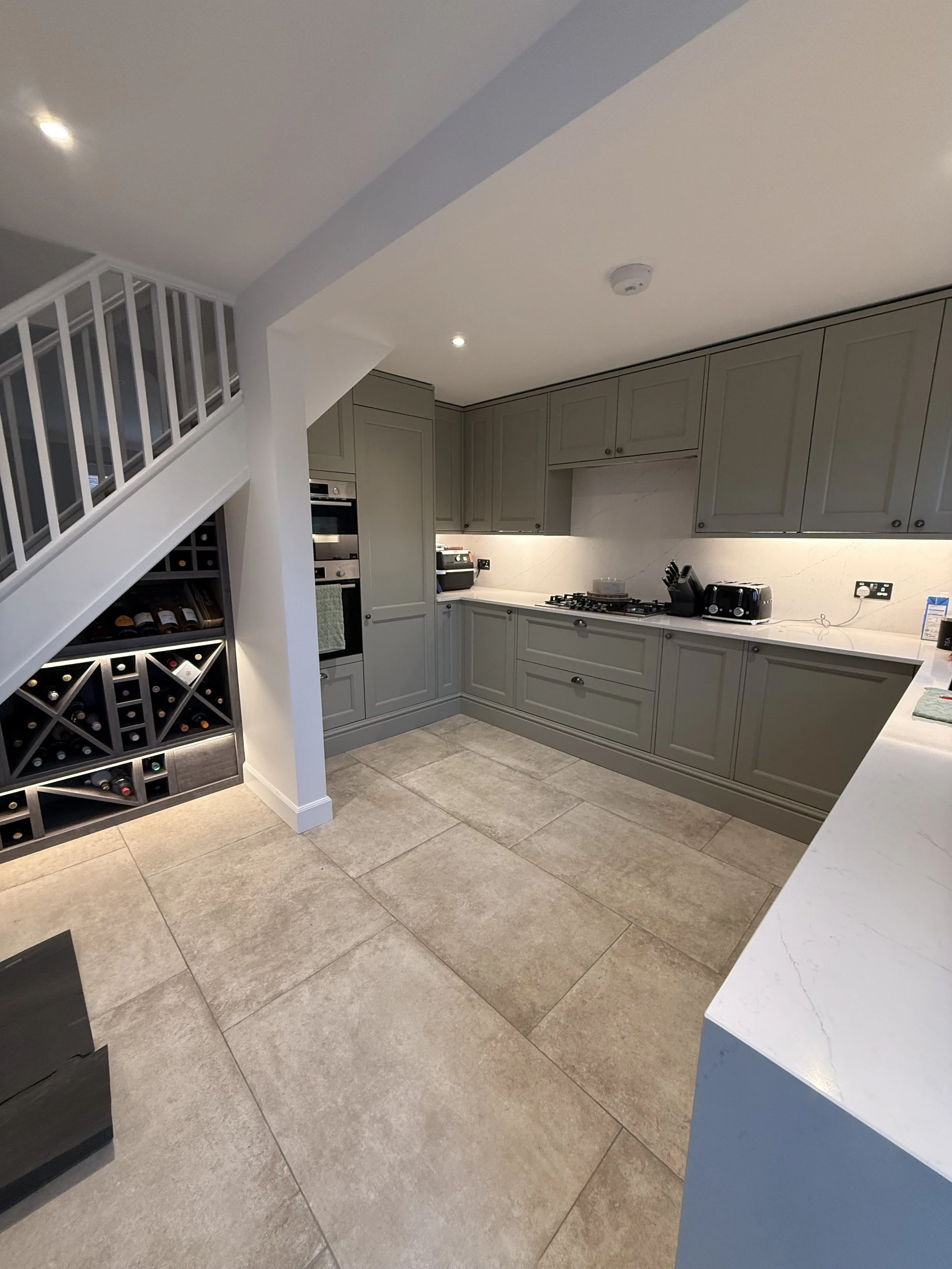 Modern kitchen with gray cabinets, tiled floor, and a wine rack under the staircase.
