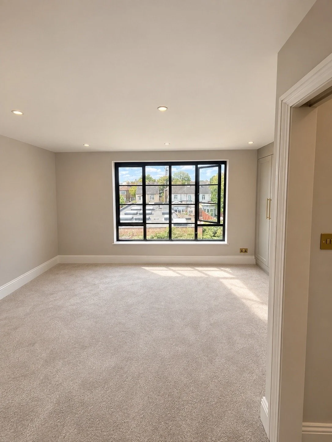 Empty room with beige carpet, white walls, large window with black grid, and ceiling lights.