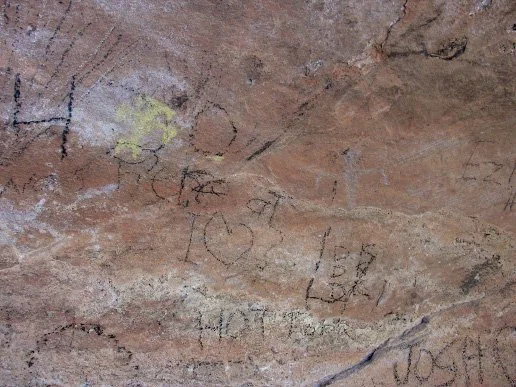 This pictograph panel that is covered with names and initials, which is a modern activity....Note the golden pictograph figure on the panel with a faint gray figure to his right.(There is no sign stating that this is a protected site.)