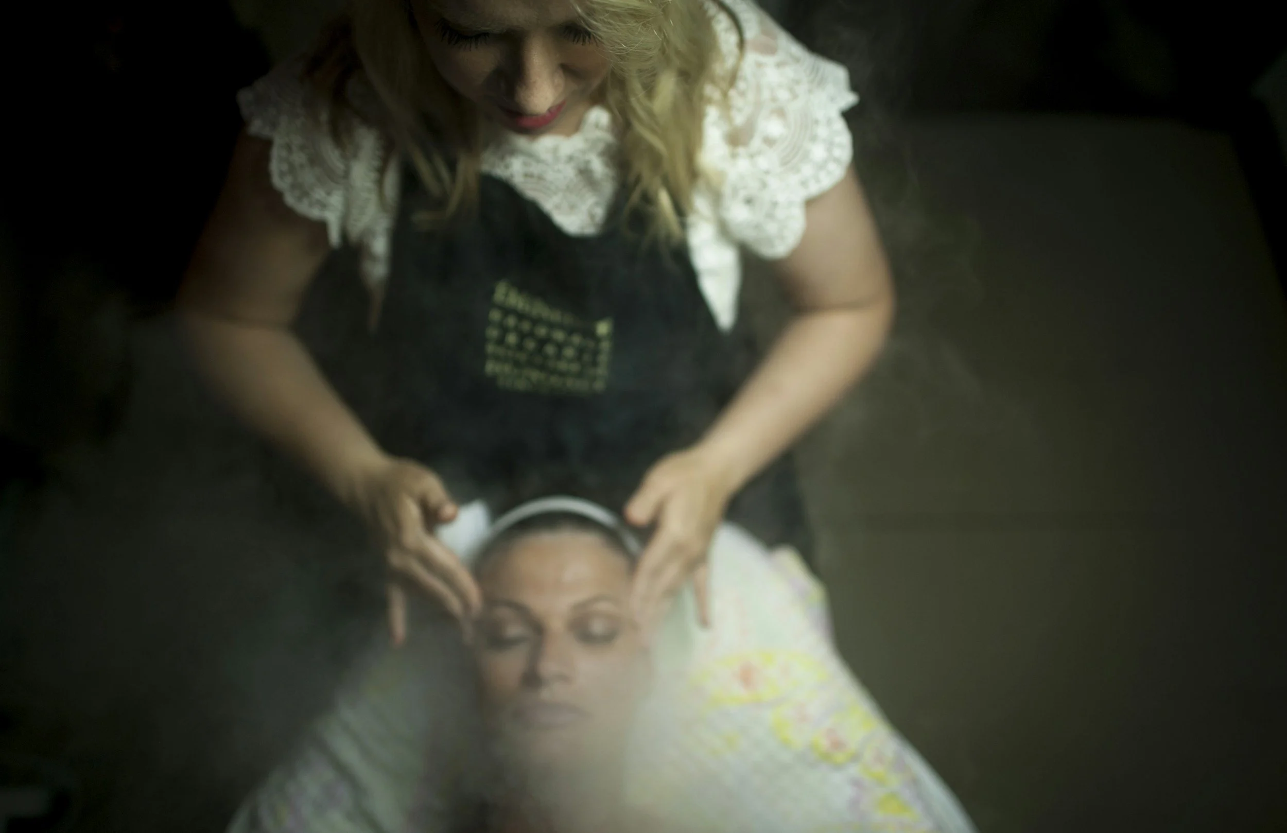 A woman receiving a facial massage, lying down with her eyes closed, while a beautician or therapist applies pressure to her face.