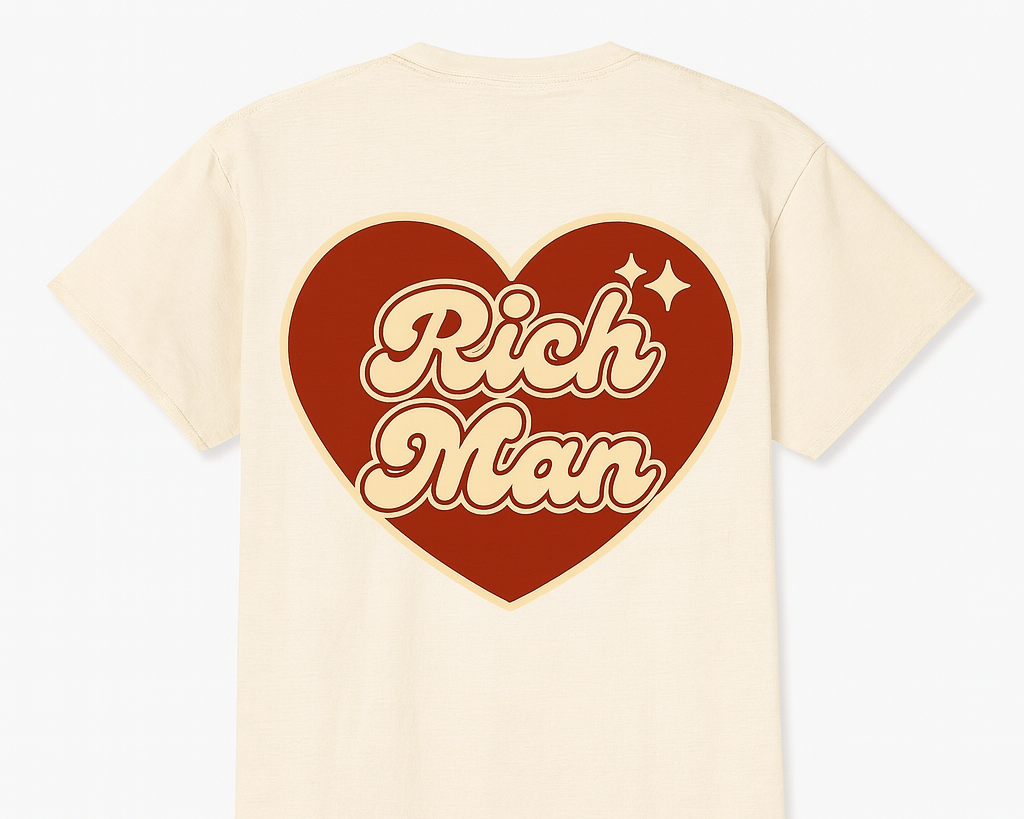 A beige T-shirt featuring a large red heart graphic with the text "Rich Man" inside, accompanied by a small sparkle icon.
