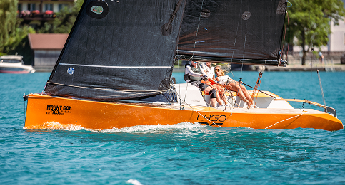 A orange and black sailboat with crew members sailing on a body of water.
