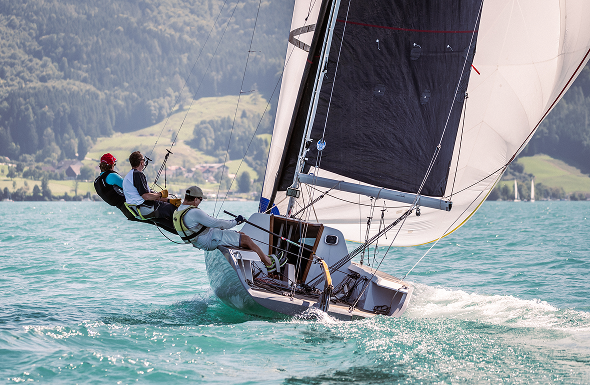 Sailboat with four crew members racing on a lake with hills in the background.