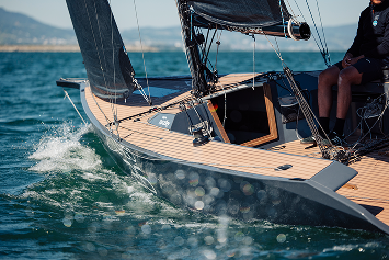 A sailboat navigating through water with two people on board, one sitting at the back.