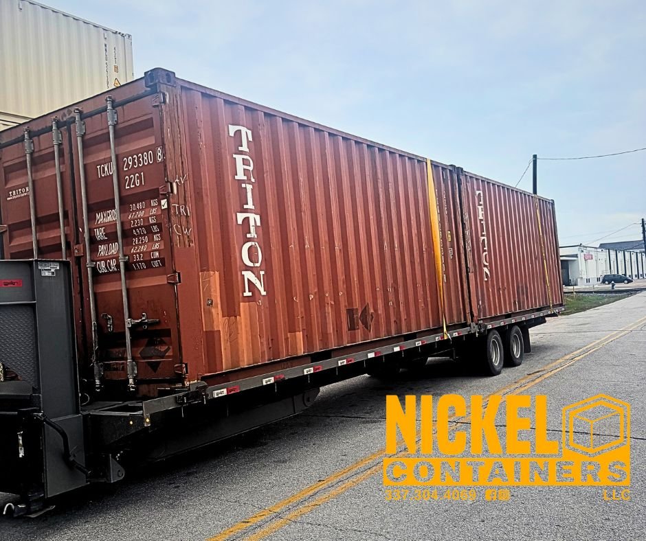 A large red shipping container on a flatbed trailer parked on a street with buildings and power lines in the background.