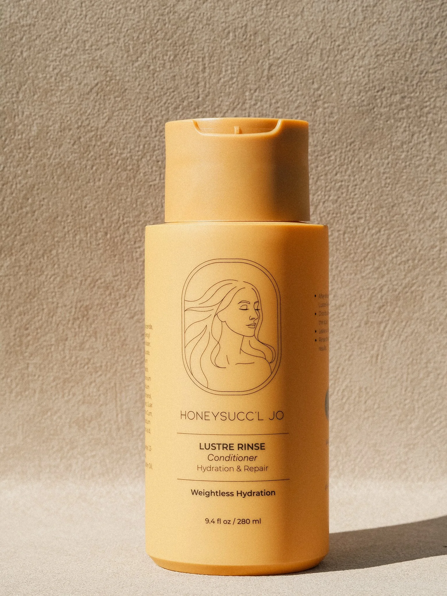 A beige bottle of HONEYSUCC'L JO Lustre Rinse Conditioner with a line drawing of a woman with flowing hair on the front, placed against a textured background.