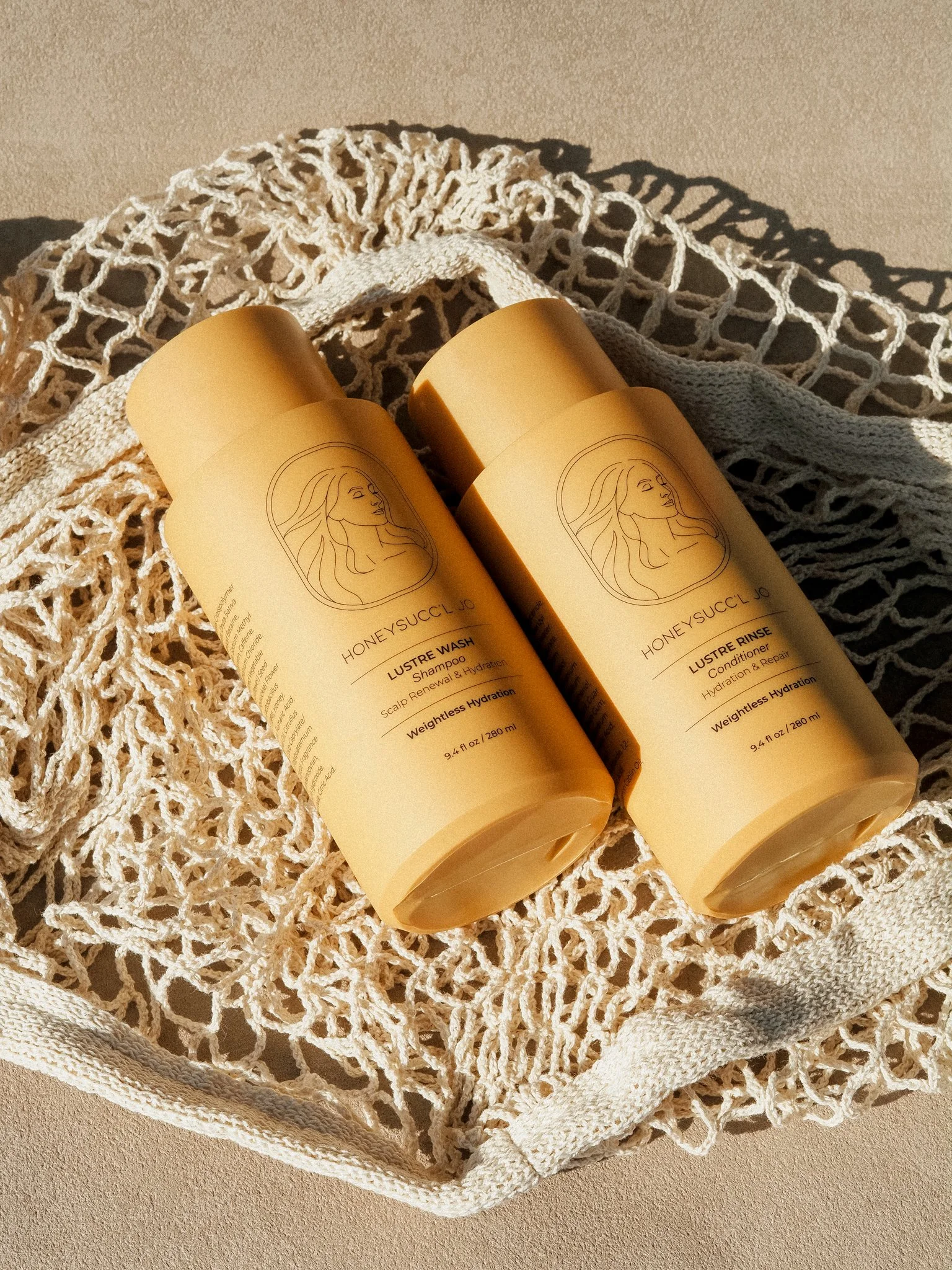 Two bottles of HONEYSUCC'L JO hair care products, a shampoo and conditioner, placed on a netted cloth in sunlight.