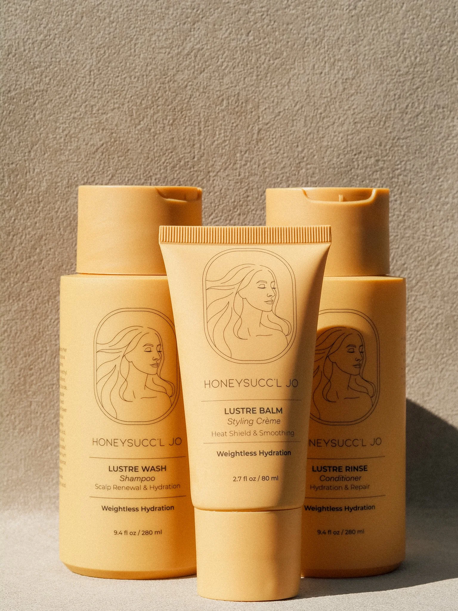 Arrangement of four hair care products from HONEYSUCC'L JO, including shampoo, styling crème, and conditioner, in beige packaging with illustrated woman on labels.