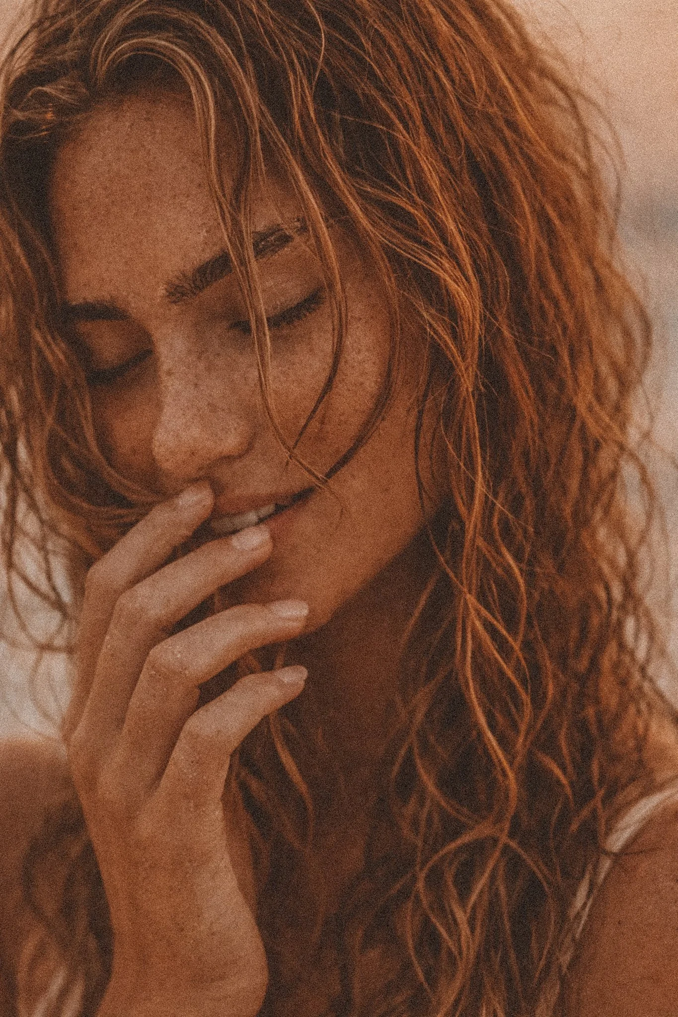 A close-up of a woman with red, wavy hair and freckles, with her eyes closed and her hand near her lips. HONEYSUCC'L JO HAIRCARE